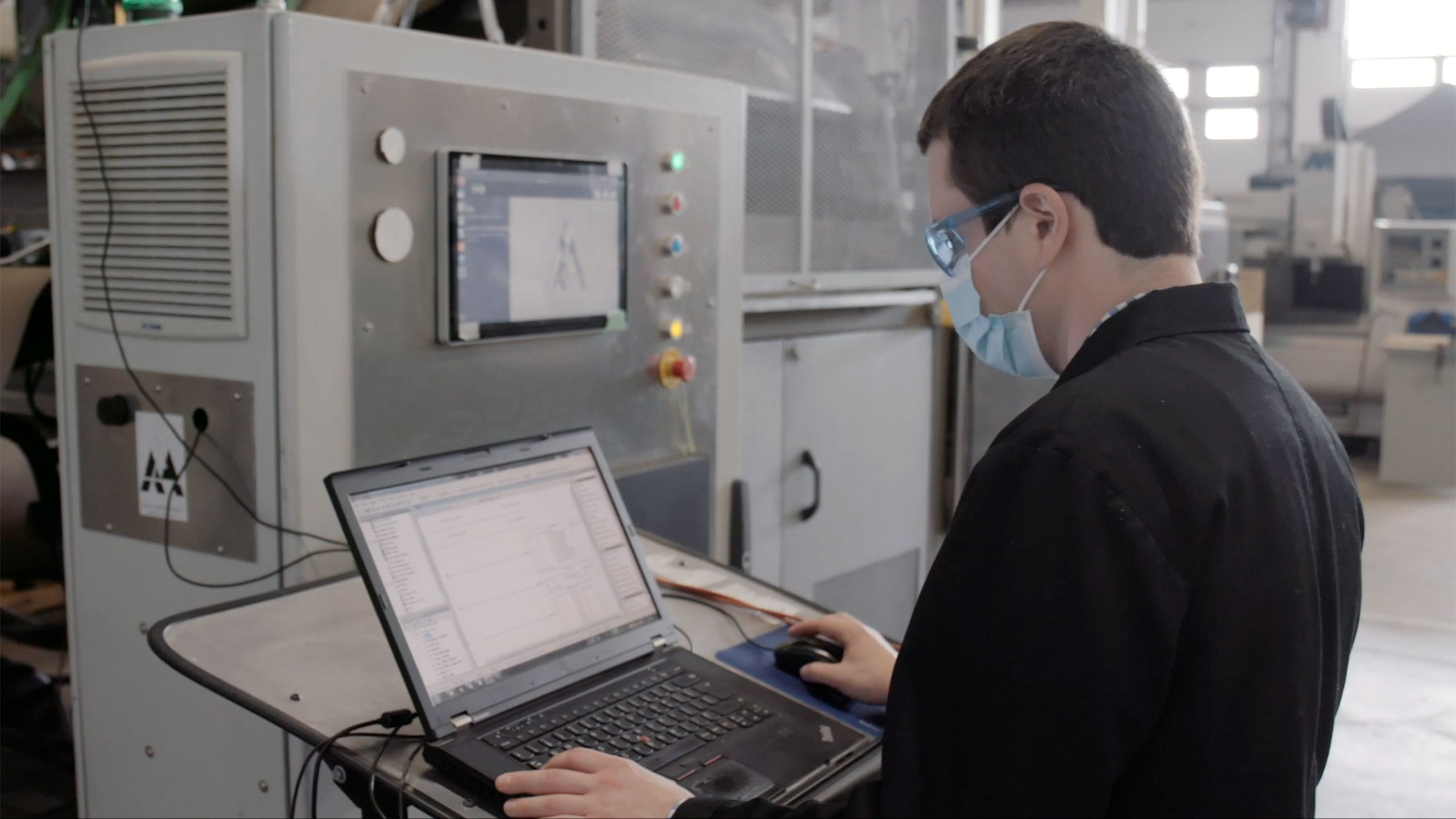 A picture of a student in a black lab coat operating his computer inside a facility. 